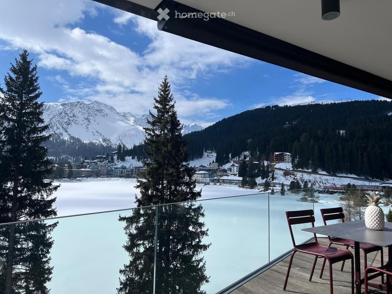 glass railing, wooden floor, table with chairs, glass table top, view of snowy mountains and lake