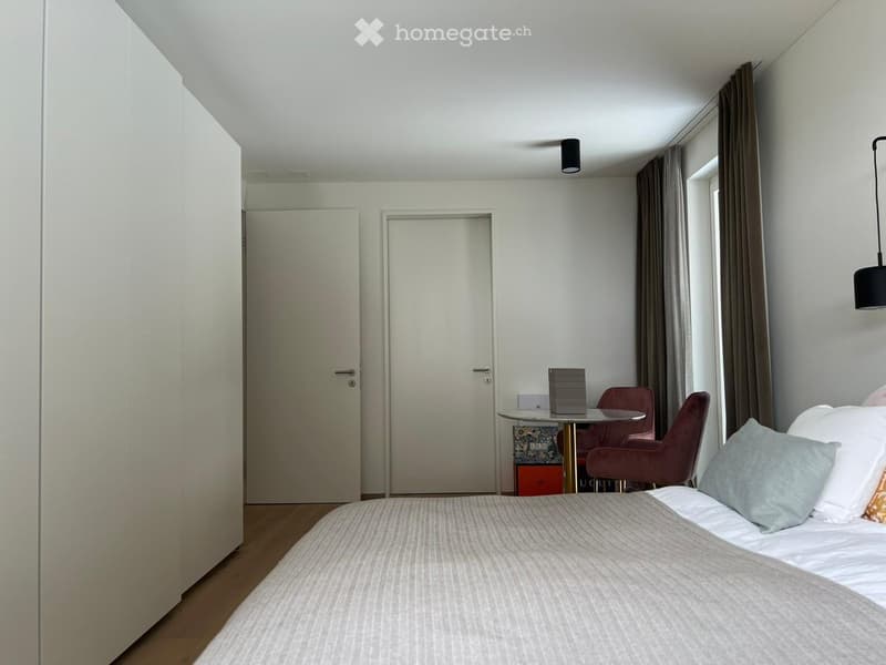 modern bedroom with white walls, wooden floor, large bed, two doors, small table with two chairs, lamps