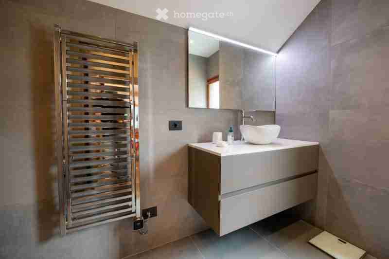Modern bathroom with a sleek sink, mirror, and cabinet. The walls are tiled in neutral tones, and the floor is tiled as well.