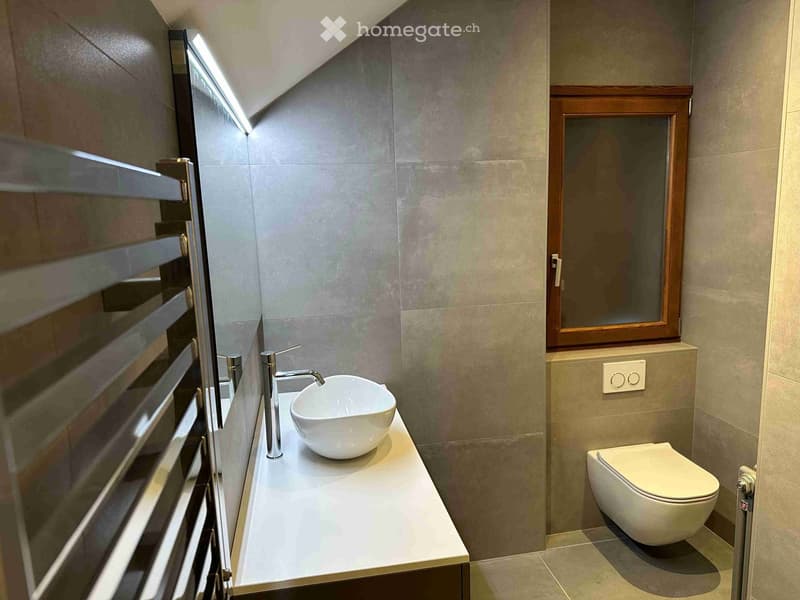Modern bathroom with a white sink, sleek faucet, and a toilet. Features a large window with wooden frame and a built-in shelf above the toilet.