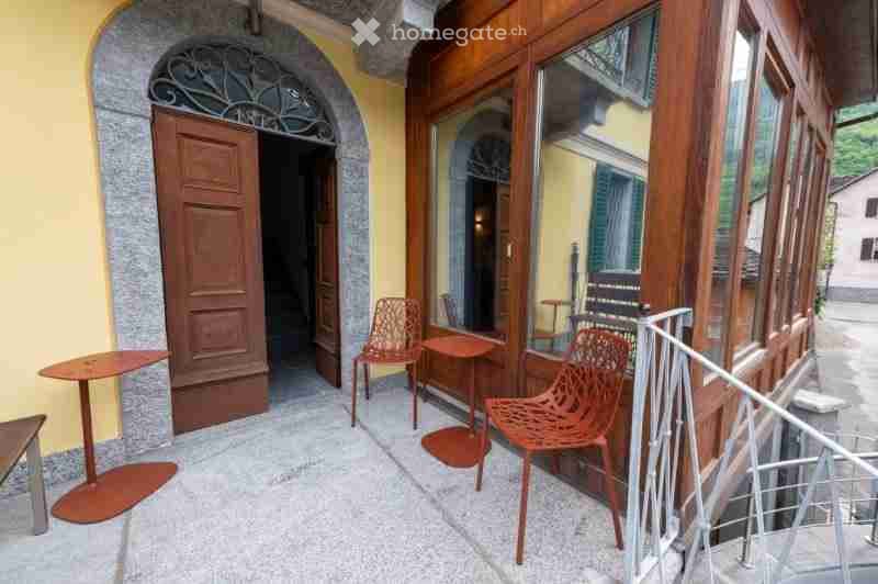 Balcony with wooden railings, glass windows, and outdoor seating including tables and chairs.