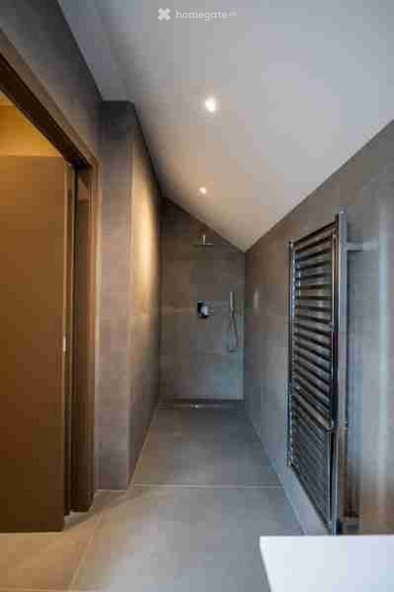 Modern hallway with sleek, contemporary design, featuring grey tiled walls and floor, recessed lighting, and a built-in towel rack on one side.