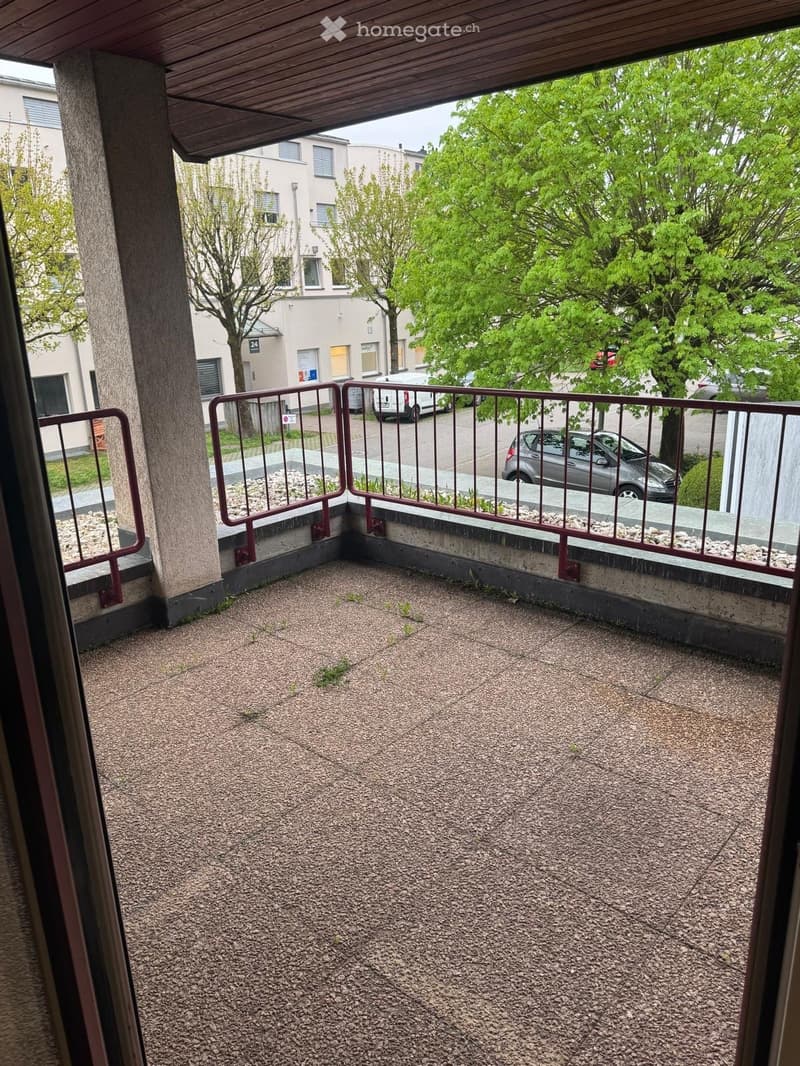Balcony with gravel flooring, metal railing, and a view of a residential area with trees and parked cars.