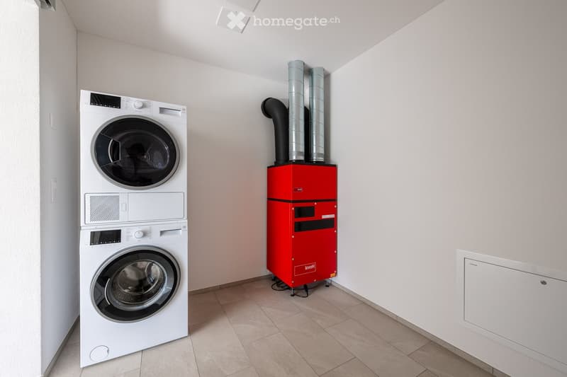 A laundry room with a washing machine and dryer stacked together, and a large red ventilation system in the corner.