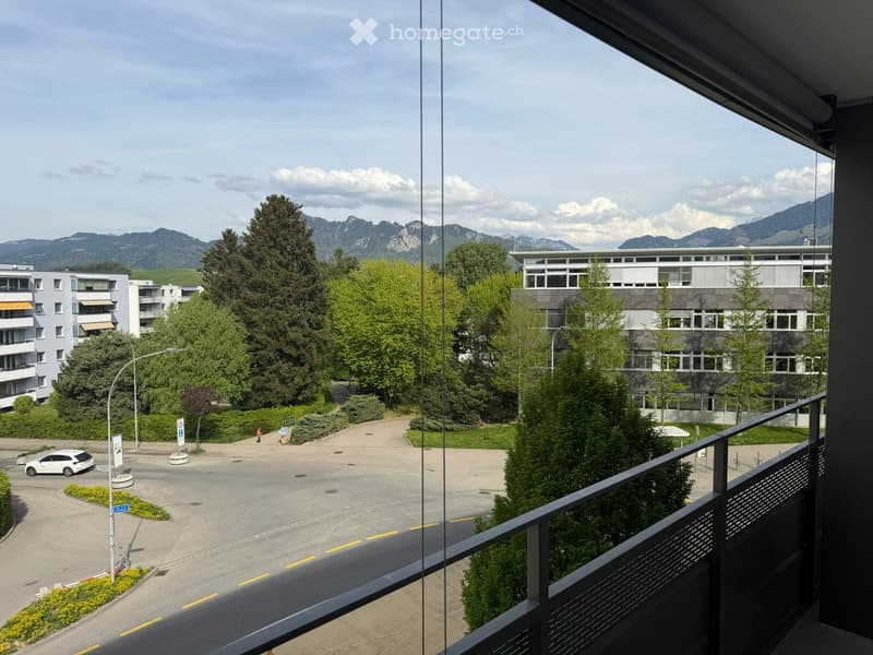 Balcony overlooking a landscaped area with trees, buildings, and distant mountains.