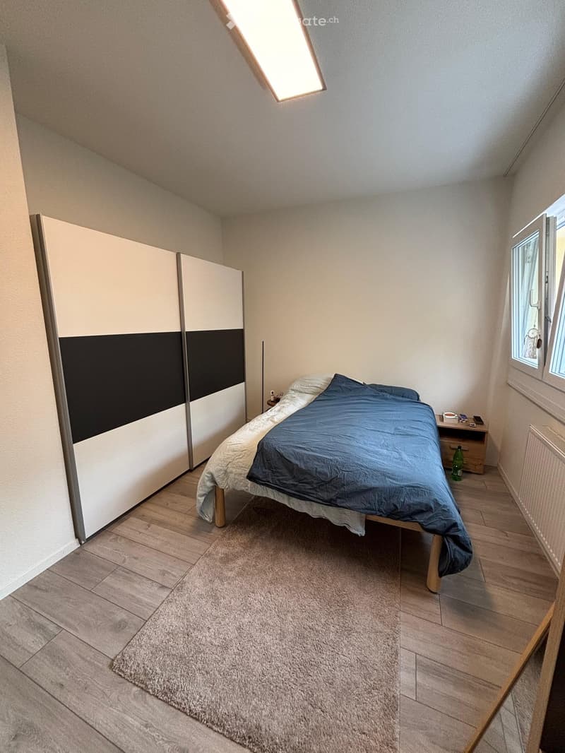 Cozy bedroom with wooden flooring, a large bed with blue bedding, a modern wardrobe, a nightstand, and a small rug.