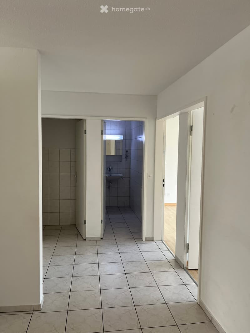 Empty hallway with tiled floor and white walls, leading to a small bathroom and another room.