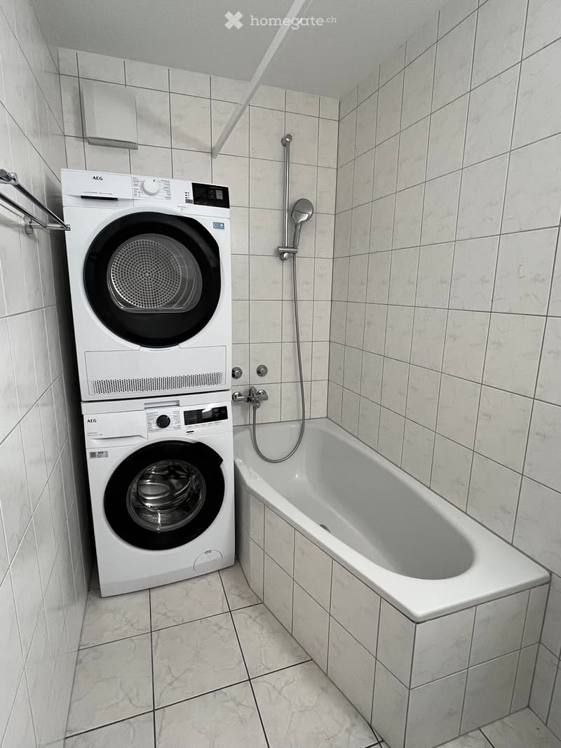 Bathroom with a bathtub and a stacked washing machine and dryer unit.