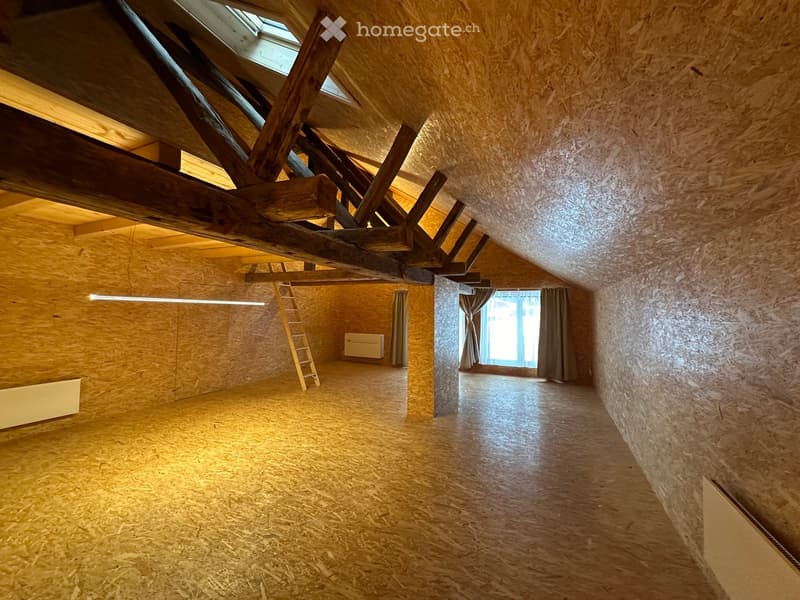 Empty attic space with wooden beams, exposed wooden floor, and a small window with curtains. Ladder leading to the attic is visible.