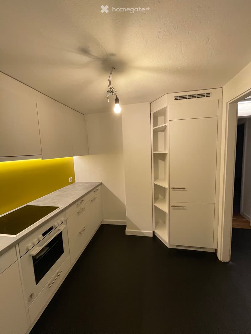 Modern kitchen with white cabinets, a built-in oven, and a sleek countertop. Features include a bright yellow backsplash and a hanging light fixture.