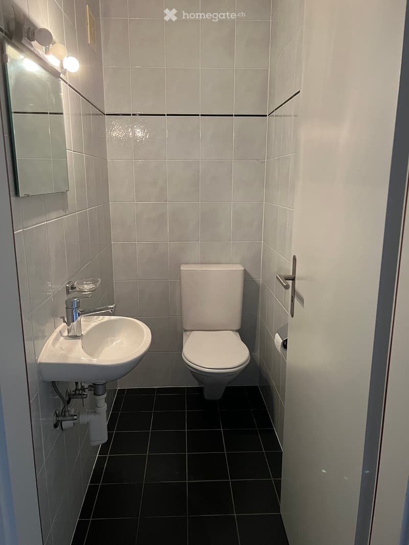 Modern bathroom with white tiles, a white sink, chrome faucet, toilet, and a mirror with built-in lighting.
