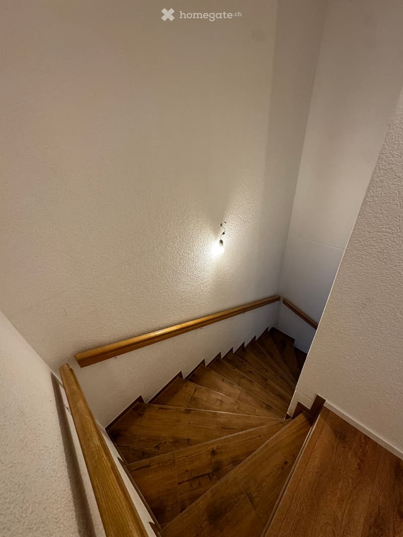 Wooden staircase with wooden handrails and a single light fixture on the wall.