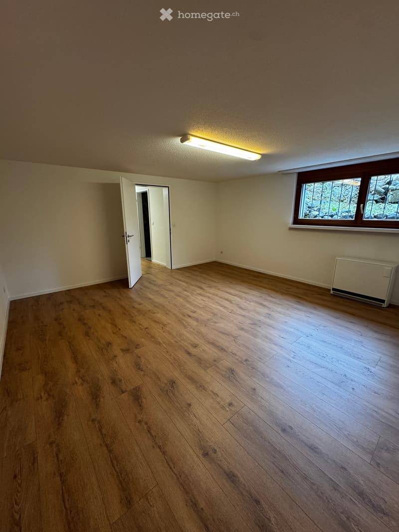 Empty room with wooden flooring, white walls, a window with decorative bars, and a radiator on the wall.