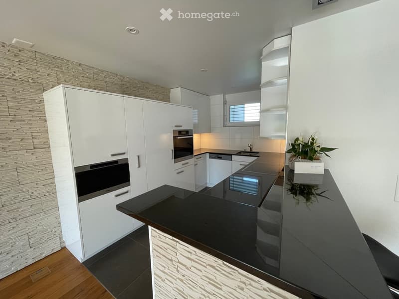 Modern kitchen with white cabinets, black countertops, built-in oven, and a stone accent wall.