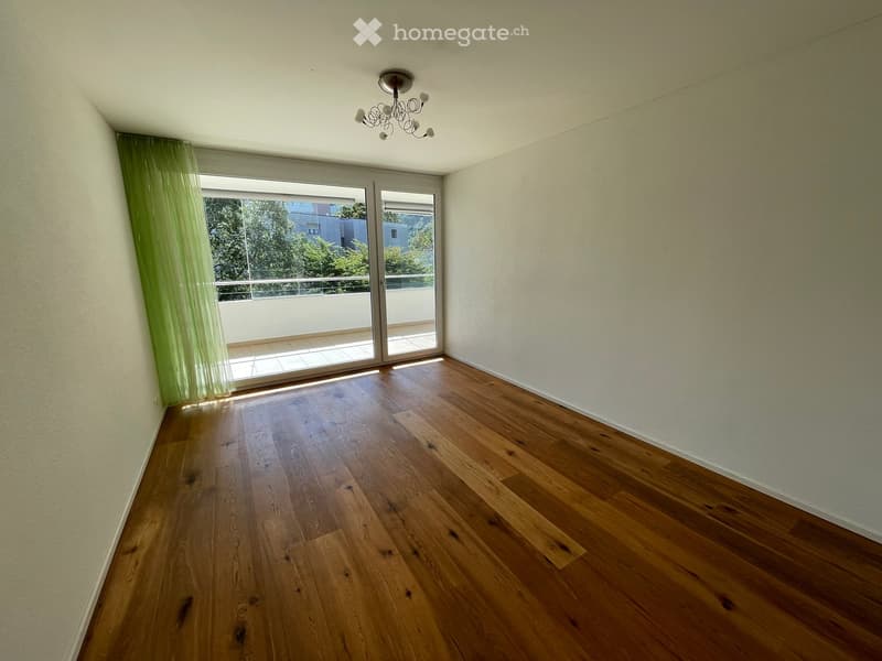 Empty room with wooden flooring, large sliding glass doors leading to a balcony, and a chandelier light fixture.