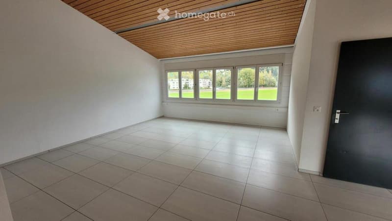 Empty room with white walls, tiled floor, large windows, and a wooden ceiling.