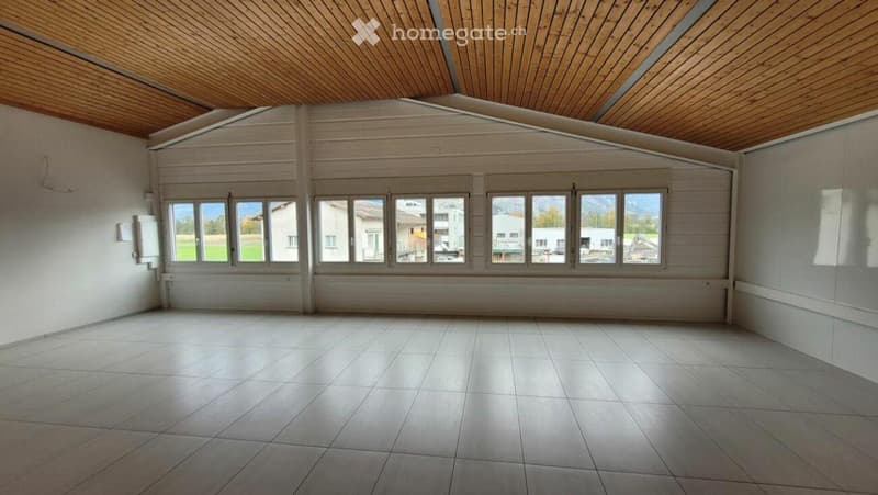 Empty room with tiled floor, wooden ceiling, and large windows offering a view of the landscape.