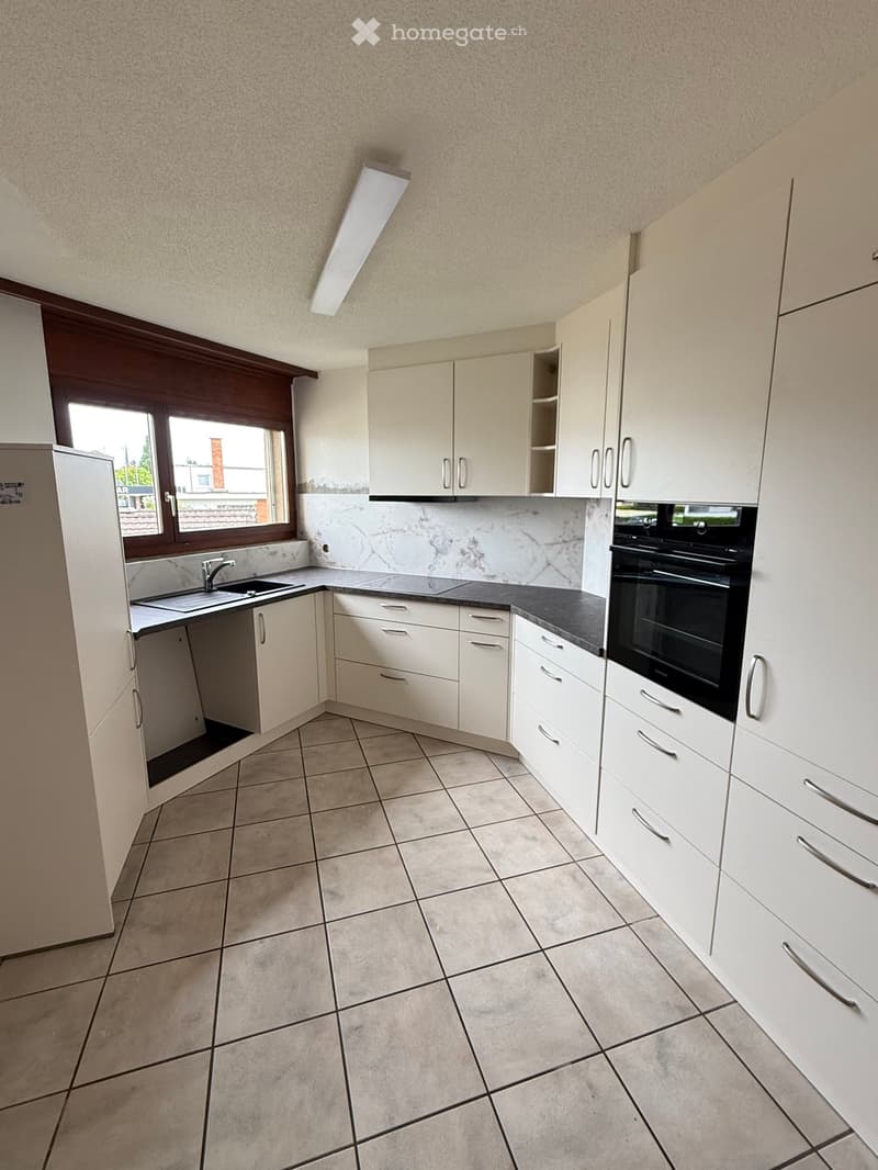 Modern kitchen with white cabinets, tiled floor, and black countertops. Features a sink, faucet, and built-in oven.