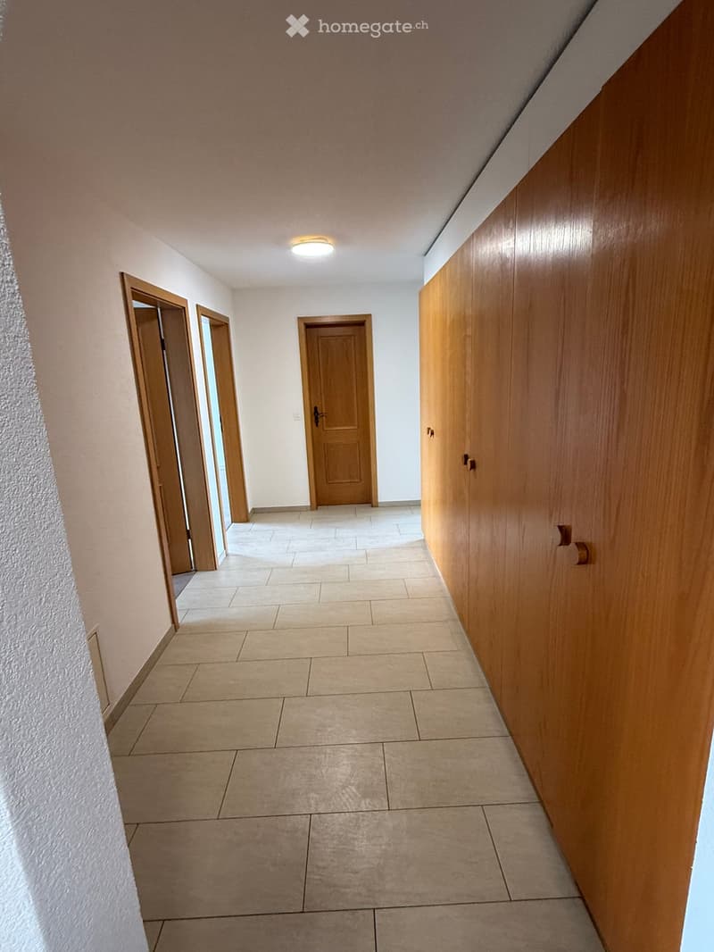 Empty hallway with tiled floor, wooden doors, and built-in wooden cabinetry on one side.