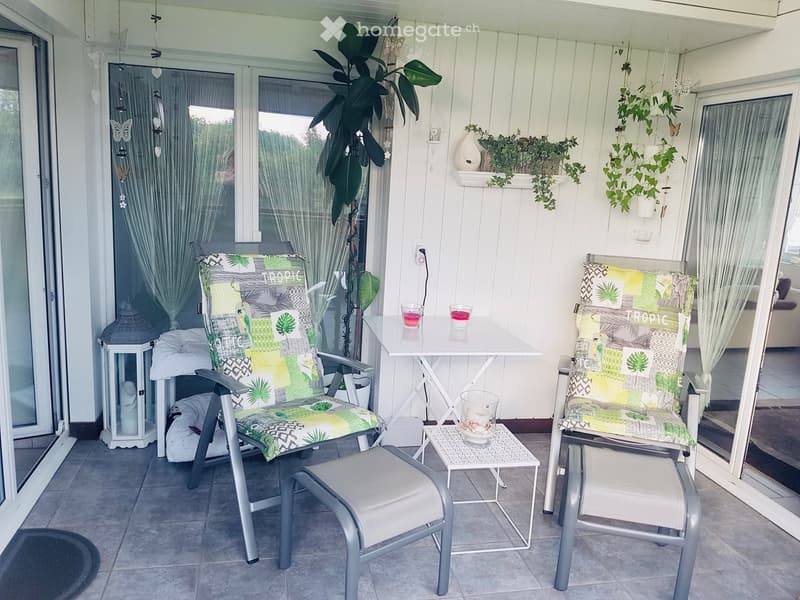 Balcony with two chairs, a small table, a stool, a lantern, and decorative plants.