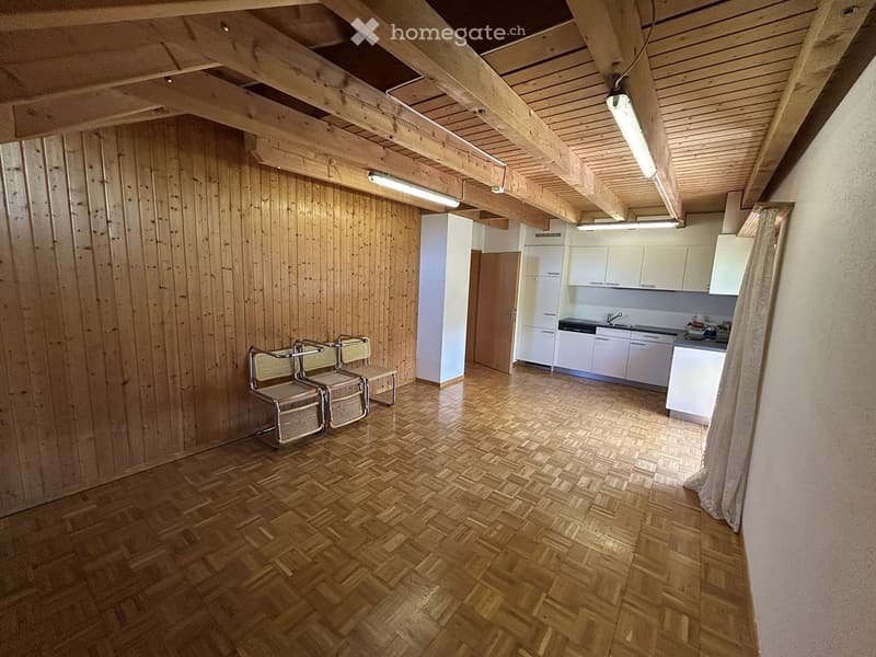 A room with wooden walls and a wooden floor, featuring two chairs, a small stool, a kitchen area with cabinets, a refrigerator, a sink, a faucet, and a stove.