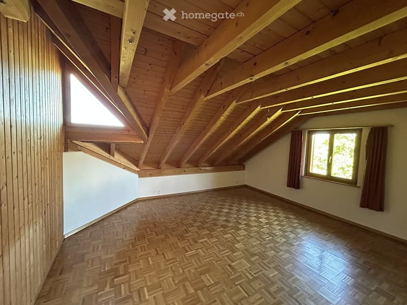Empty attic room with wooden beams, herringbone wooden flooring, and large windows with curtains.