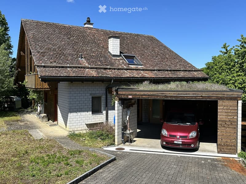 Two-story house with a tiled roof, white brick lower level, and wooden upper level. Features a covered garage with a red car parked inside.