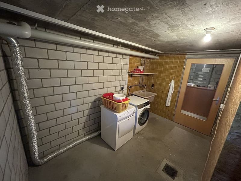 Utility room with white brick walls, concrete ceiling, washing machine, dryer, sink, and a small shelf with items.