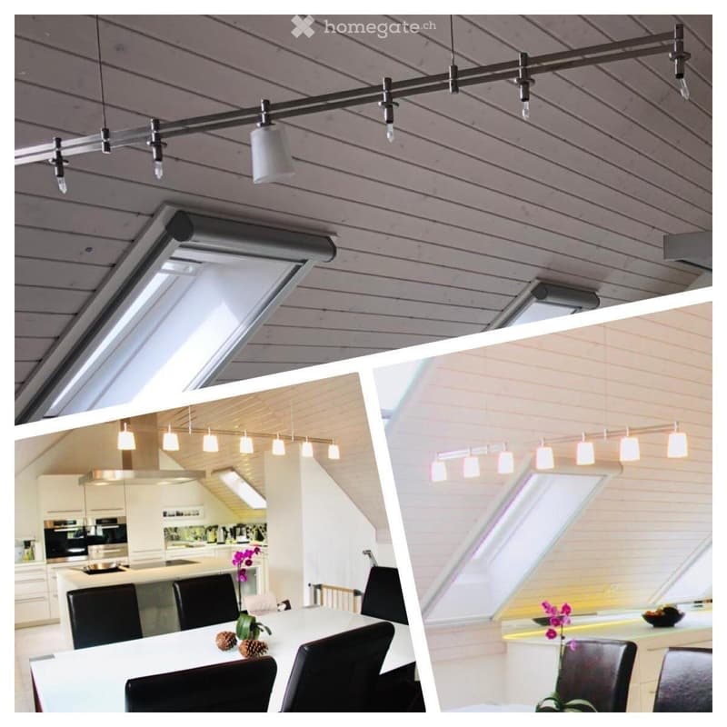 Modern kitchen with white cabinets, stainless steel appliances, and a dining area with a white table and black chairs. The ceiling features exposed wooden beams and pendant lights.