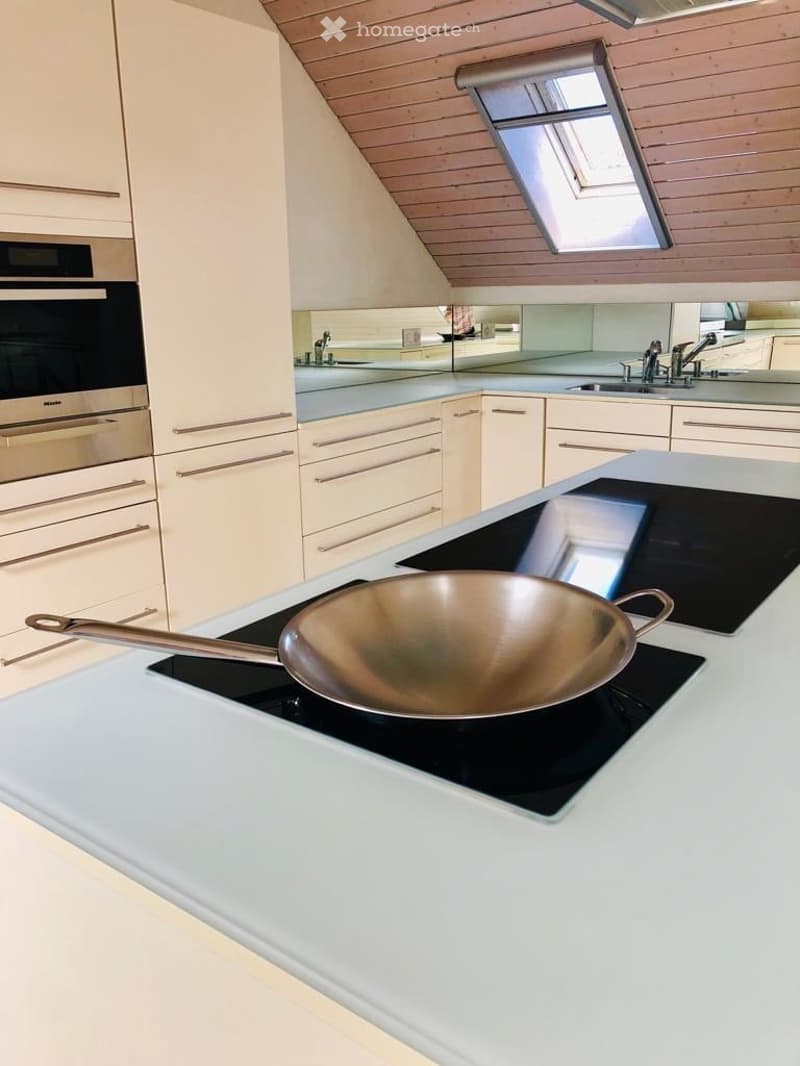 Modern kitchen with white cabinets, stainless steel appliances, and an induction stove with a frying pan on it.
