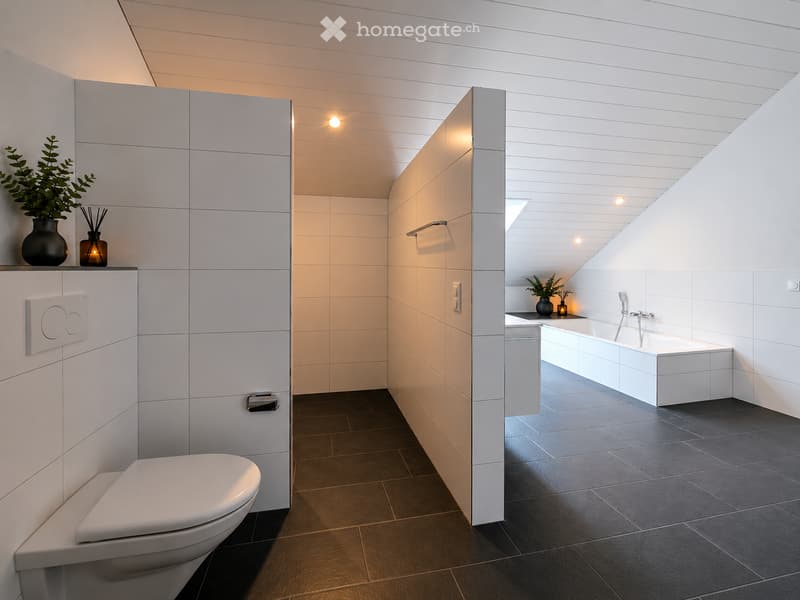 Modern bathroom with white tiles, dark floor, toilet, bathtub, and decorative plants on shelves.