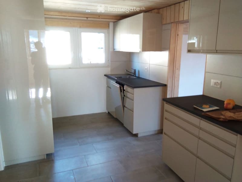 Modern kitchen with white cabinets, black countertops, and a dishwasher. The space features tiled flooring and large windows allowing natural light to enter.