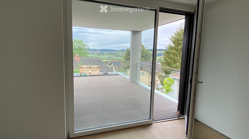 View of a modern balcony with glass sliding doors, wooden decking, and scenic countryside view.