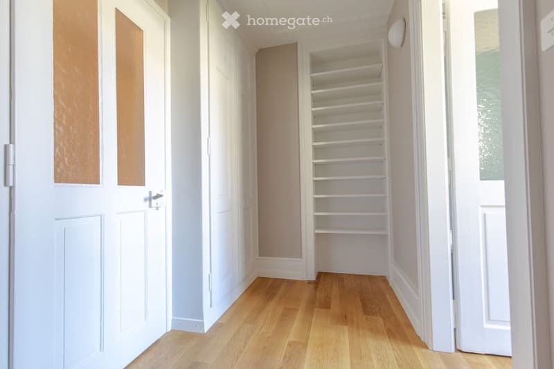 Empty hallway with wooden floor, white doors, and built-in shelves
