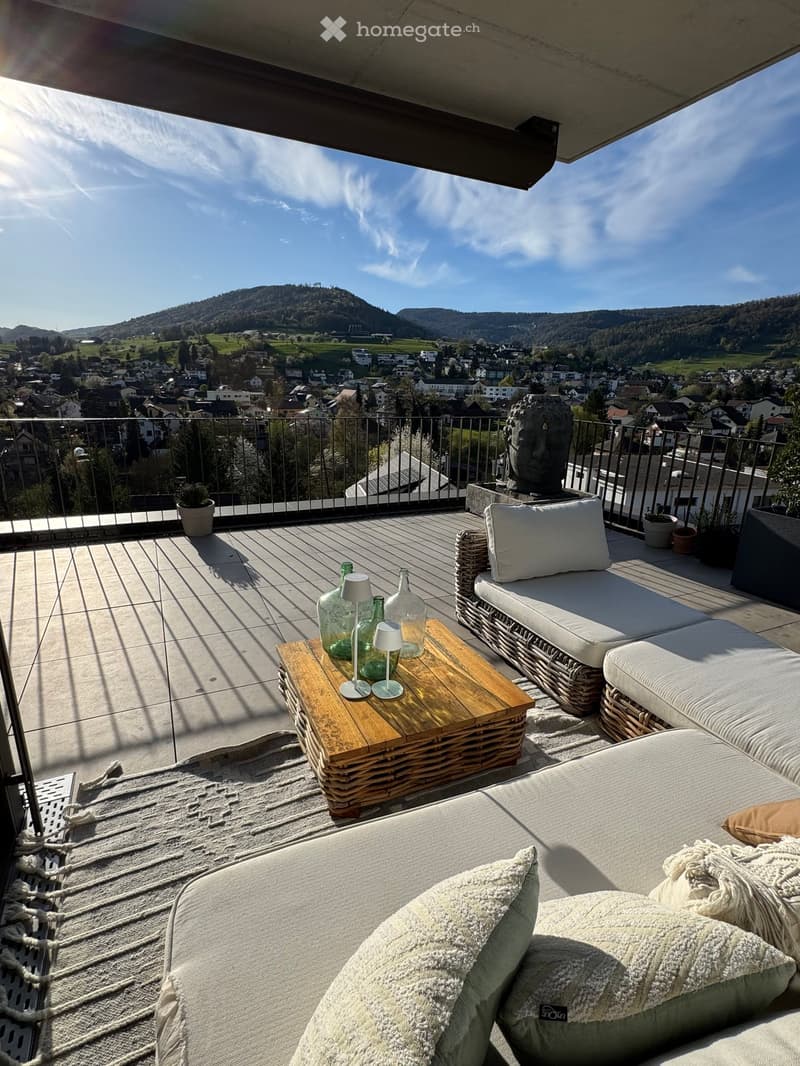 Outdoor terrace with a wooden table, wicker couches, and a view of the town below