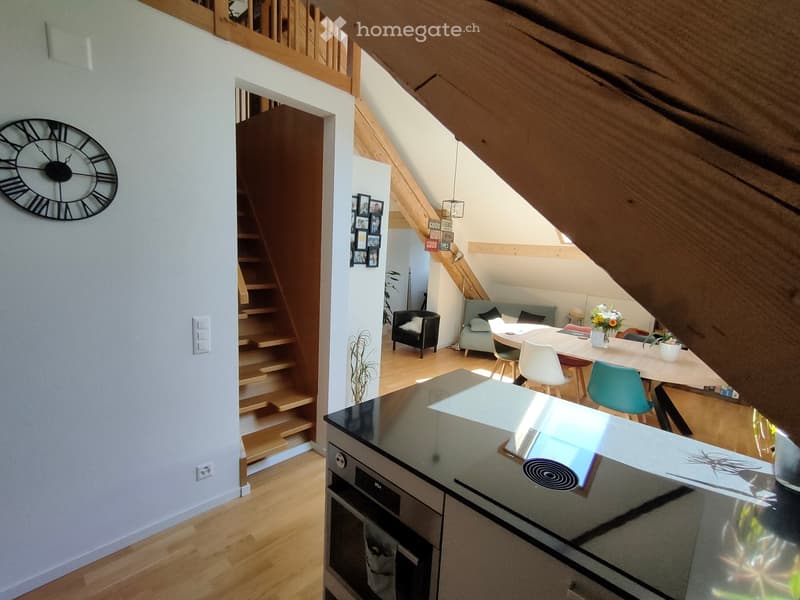 Open-plan living and dining area with wooden flooring, a staircase leading to an upper level, a modern kitchen island, a dining table with chairs, and a seating area with a sofa and armchair.
