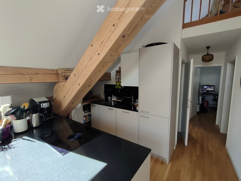 Modern kitchen with white cabinets, black countertops, and a coffee maker on the counter. A wooden staircase leads to an upper level.
