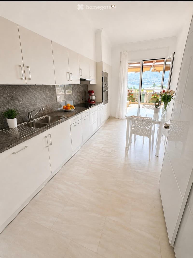 Modern kitchen with white cabinets, marble backsplash, stainless steel sink, and a dining area with a table and chairs. Offers a scenic view through large windows.