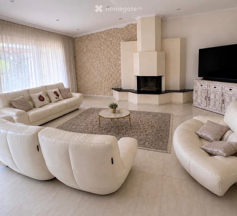 Modern living room with white leather sofas, a fireplace, a coffee table, and a television on a cabinet.