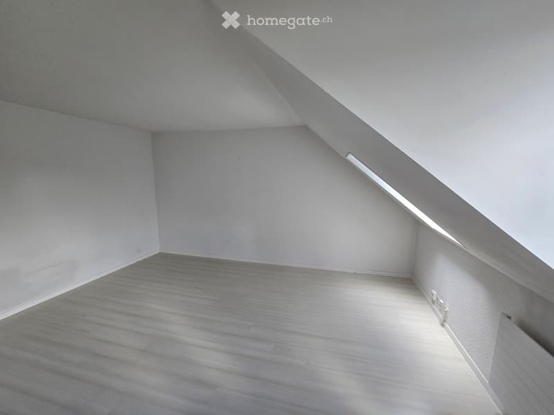 Empty attic space with wooden flooring, white walls, and a slanted ceiling with built-in lighting.