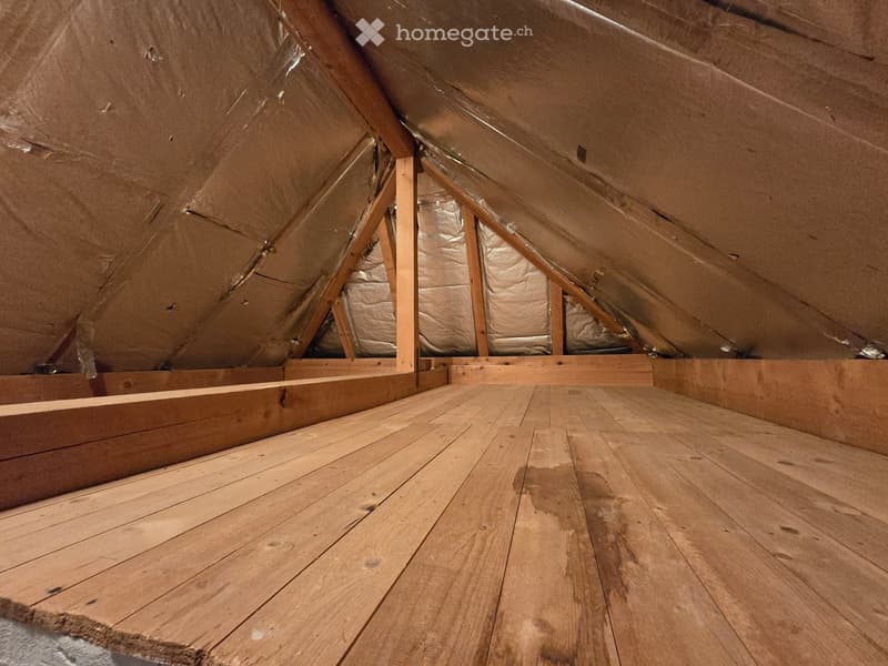 Empty attic space with wooden flooring and exposed wooden beams, insulation visible on the walls and ceiling.