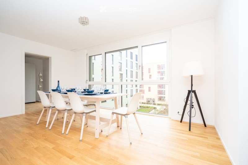 Bright dining area with white walls, wooden floor, large windows, and a modern dining set including a table, chairs, and decorative items.