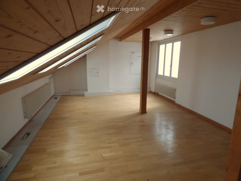 Empty attic space with wooden floors, white walls, skylights, and a central support beam.