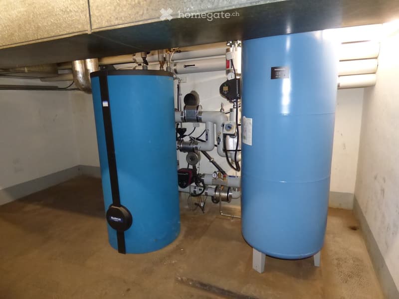 Utility room with two large blue water tanks, pipes, valves, and control units.