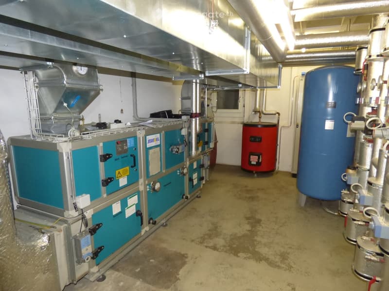 Utility room with air conditioning unit, water tank, and various pipes and valves.