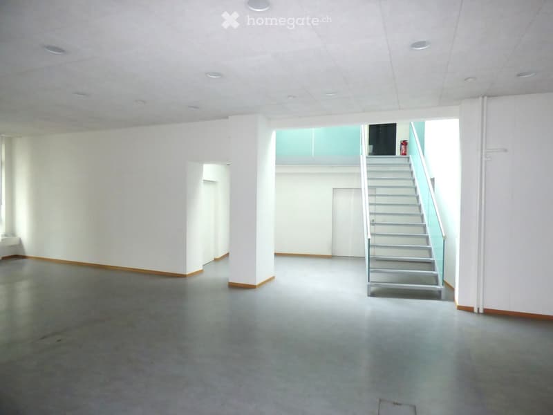 Empty room with white walls, grey concrete floor, and a staircase leading to an upper level.