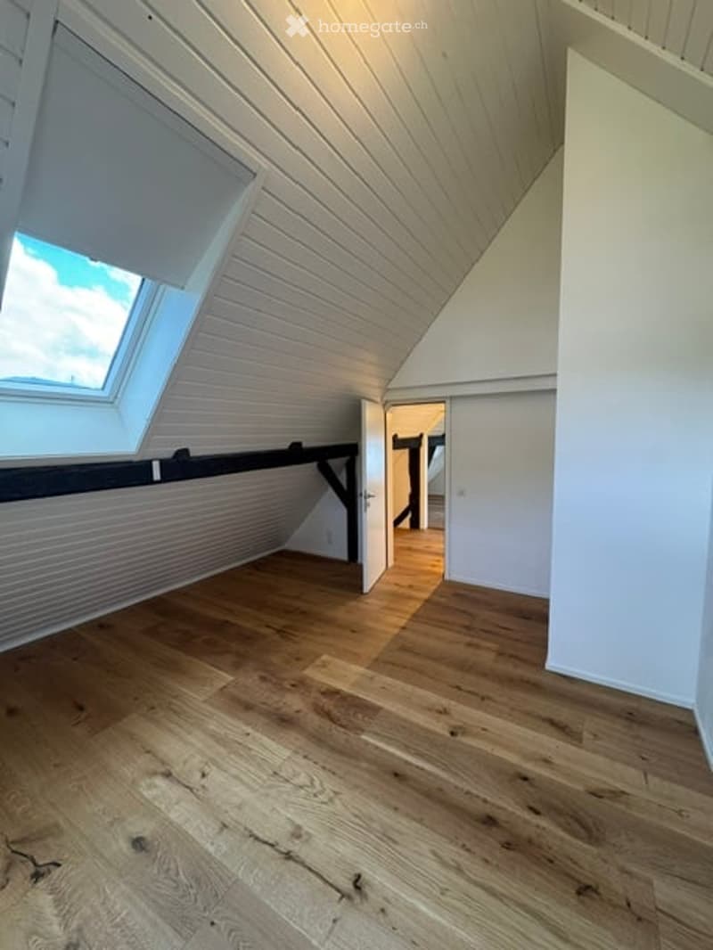 Bright, empty attic room with wooden flooring, white paneled ceiling, and skylight window. No furniture or equipment present.