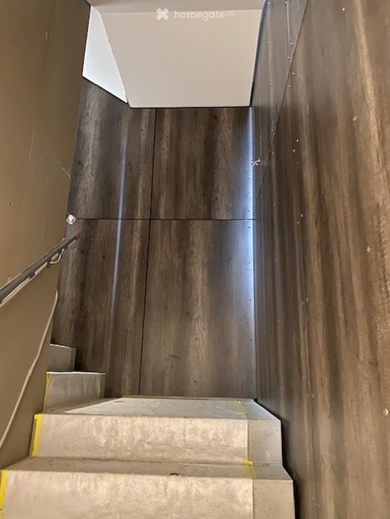 Modern staircase with wooden panel walls and a sleek metal railing, leading upwards.