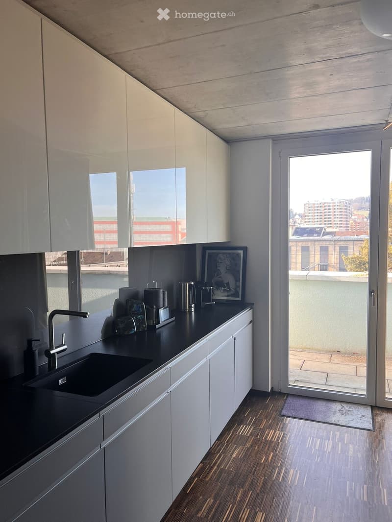 Modern kitchen with white cabinets, black countertop, and a sink. A picture frame and a cup are placed on the counter. The kitchen has a sliding glass door leading to a balcony with a city view.