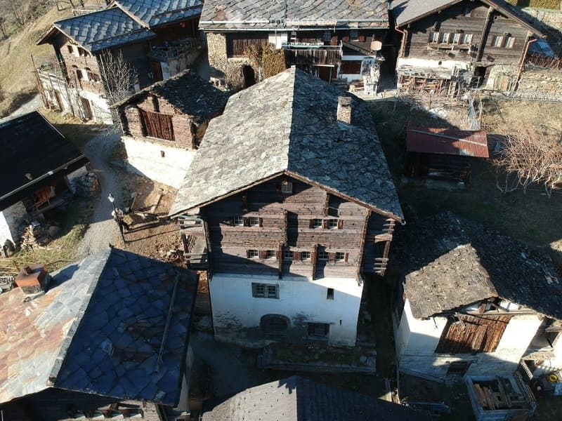 Aerial view of a rustic village with traditional wooden and stone houses, narrow pathways, and a mix of intact and partially dilapidated structures.